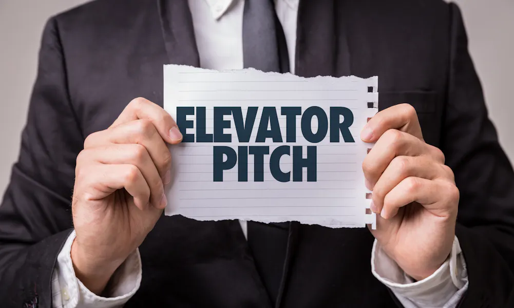 Picture of a man in a suit, holding a piece of paper that says "elevator pitch"
