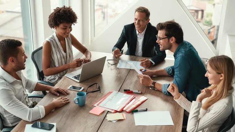 Group of young business people discussing and smiling sitting at meeting table.