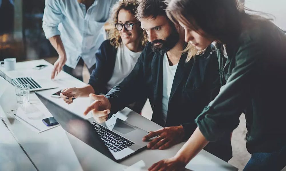 Four colleagues gathered around a laptop sharing input