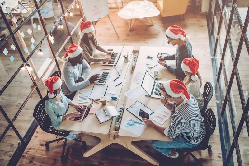 Six people working together on their laptops wearing santa hats