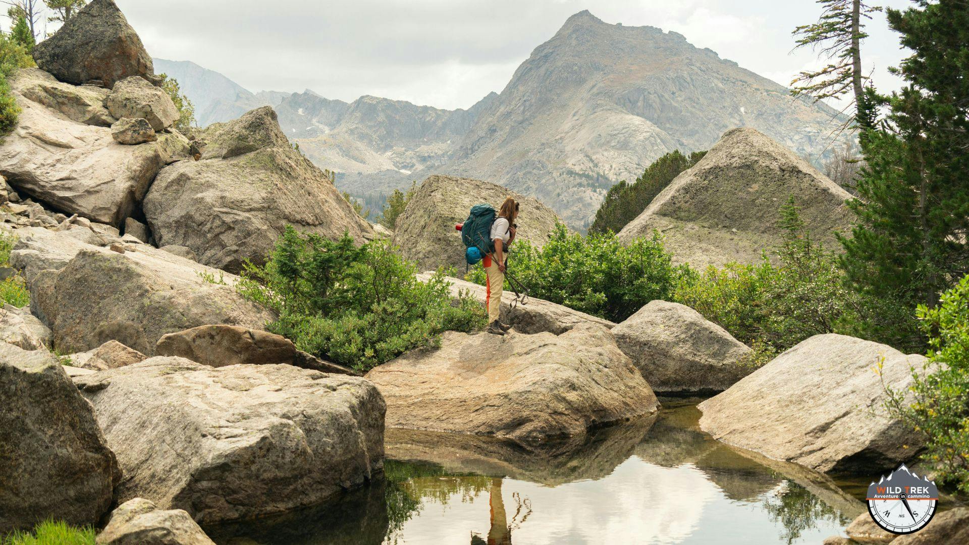 Escursionista solitario davanti ad un laghetto alpino circondato da paesaggio alpino
