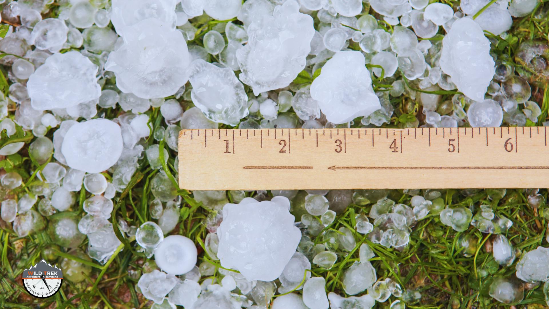 chicchi di grandine sul prato con accanto un righello
