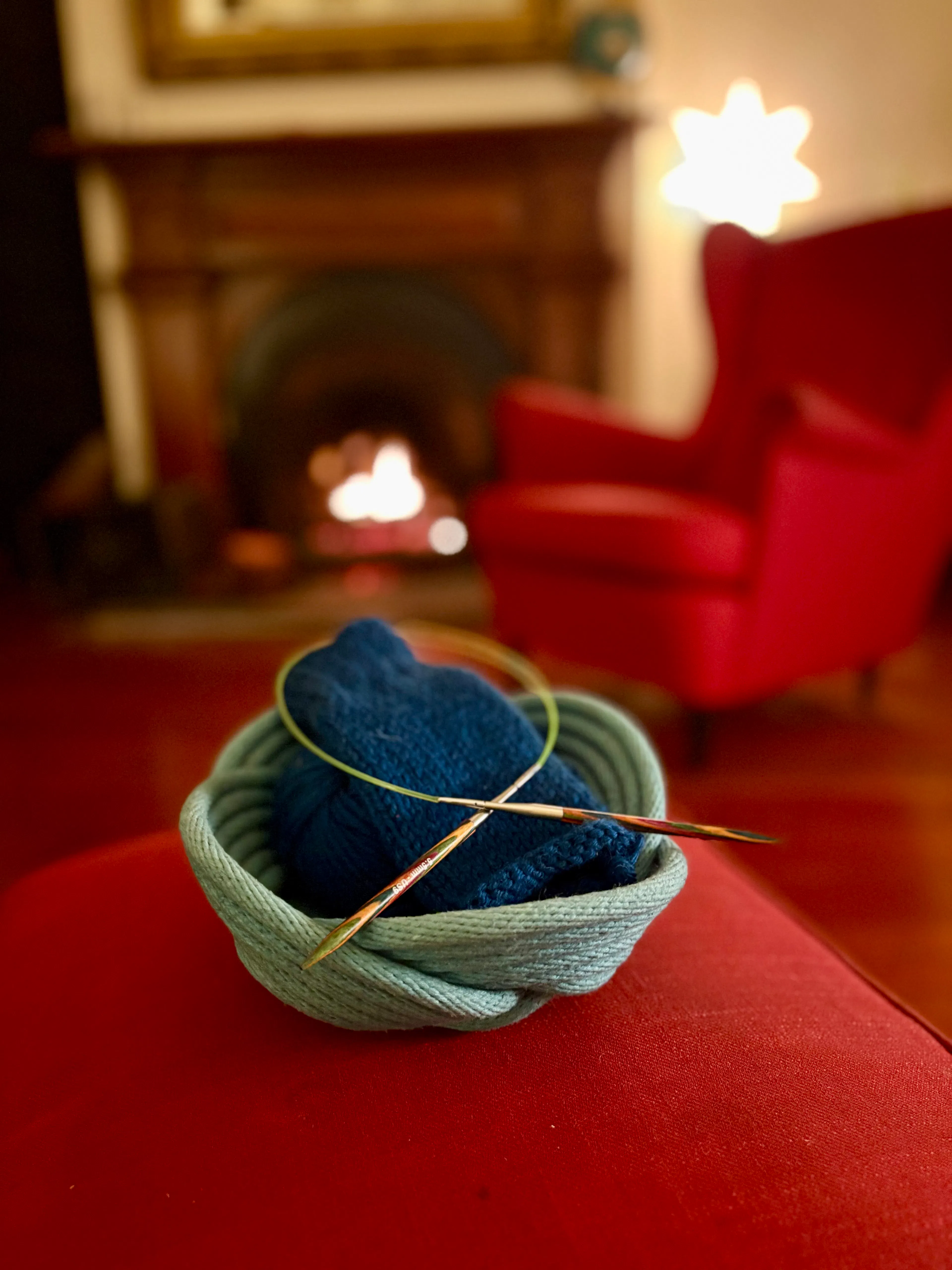 knitting in a basket in front of a lit fireplace