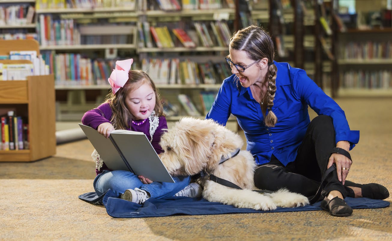 Therapy dog sitting with a woman and child in a library.
