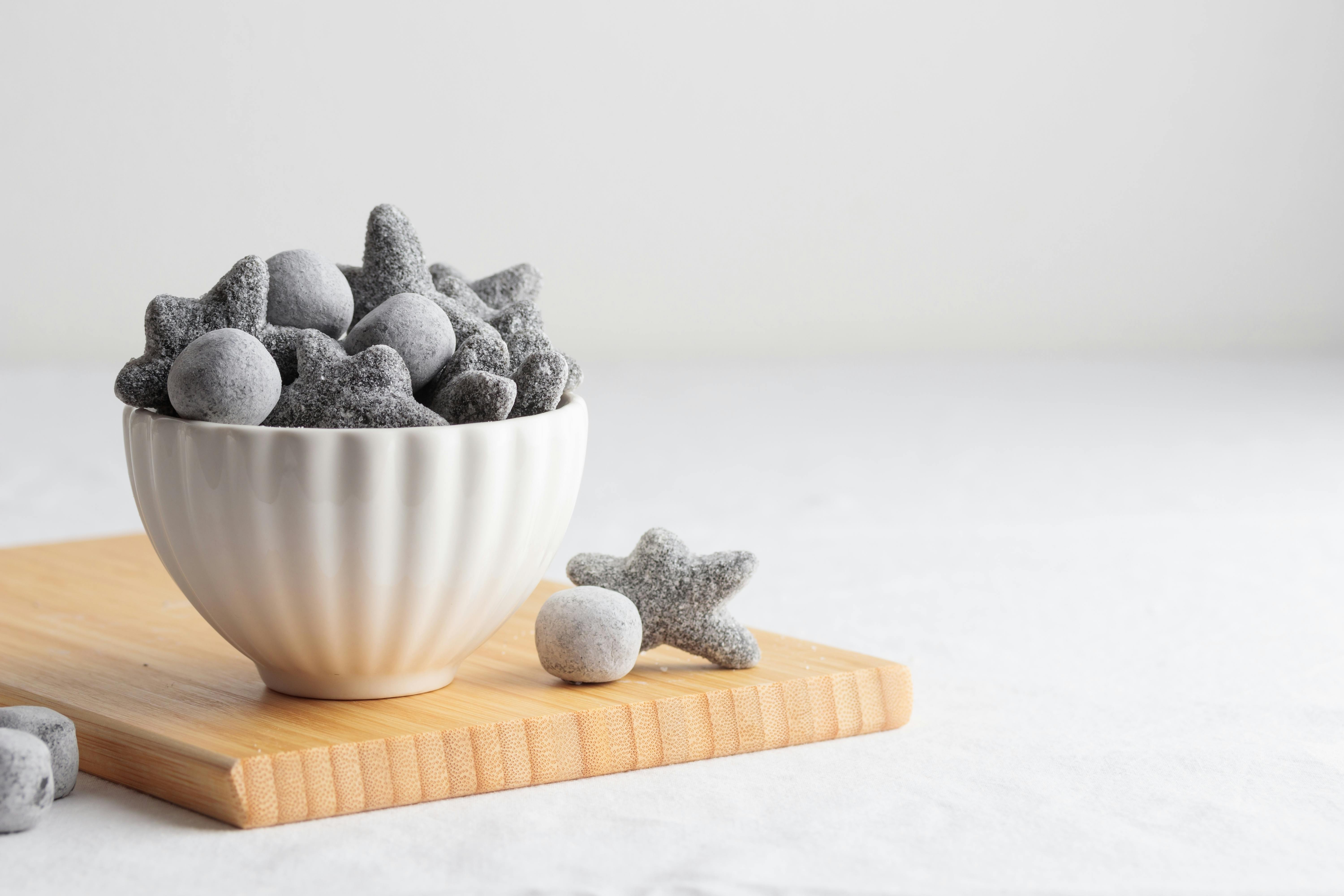 A bowl of salty licorice candy on a wooden board.