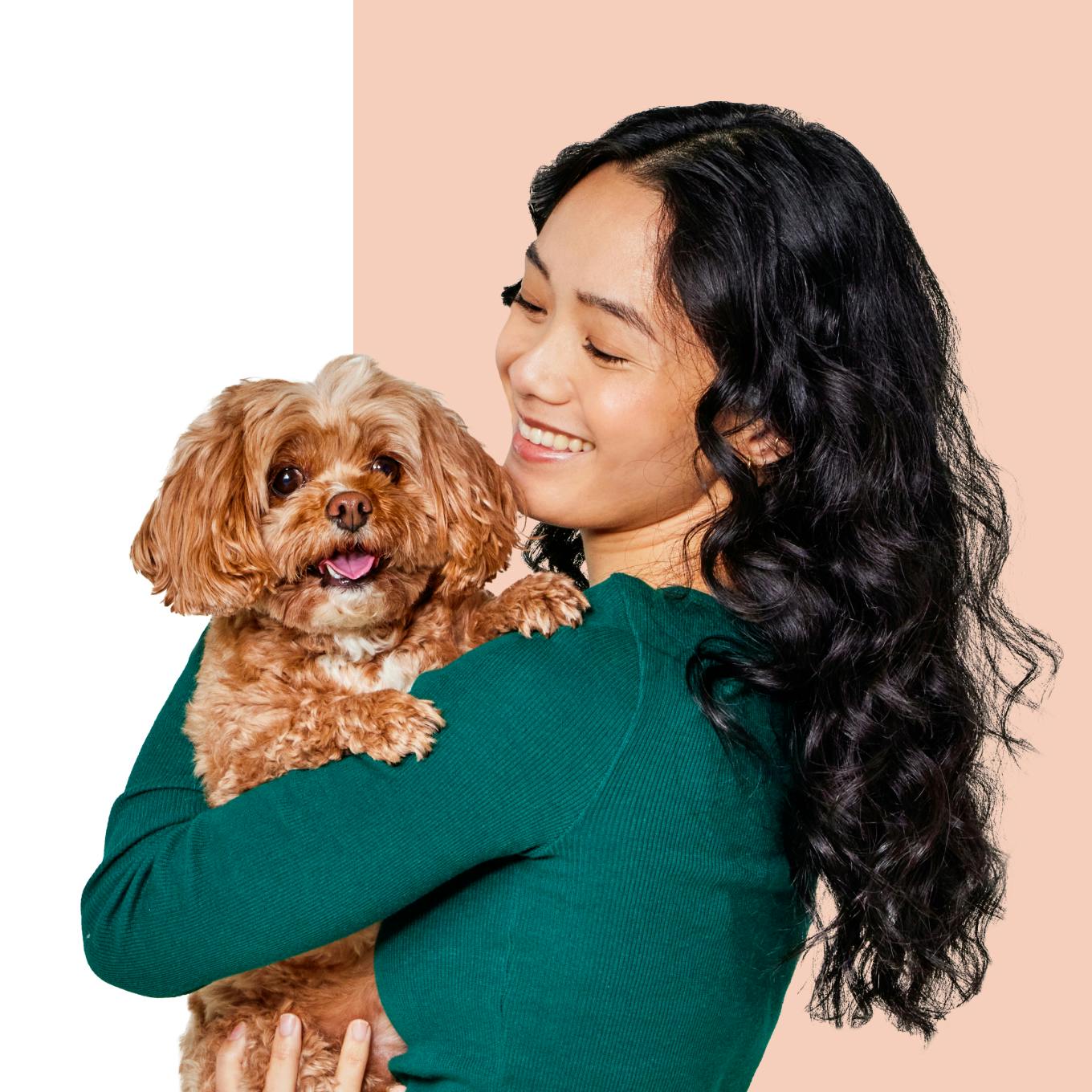 A smiling woman holding a small brown dog.