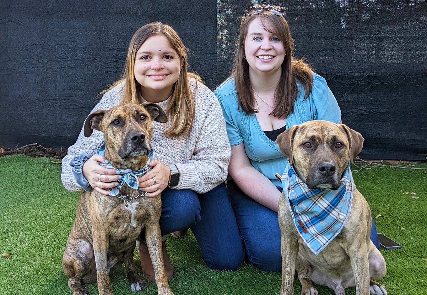 Two women posing with two medium size brown dogs