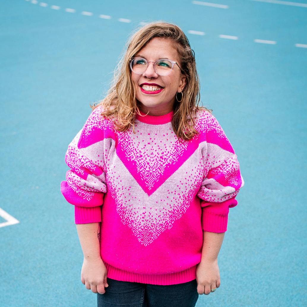 Ninia in einem pinken Pullover steht auf einem blauen Sportfeld und schaut lächelnd in den Himmel