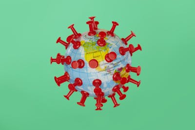 A toy globe is modeled to look like a virus cell under the microscope. It is shot on a green background and shows North America. It illustrates the concept of the pandemic affecting all areas of the globe.