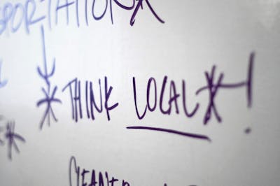 "Think local!" written on a whiteboard in dark ink.