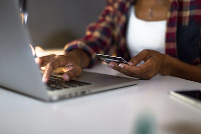 A woman has a credit card in hand while typing on a computer to make an online purchase