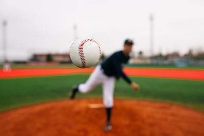 White baseball flying directly toward camera after powerful throw from blurred pitcher during baseball match on field