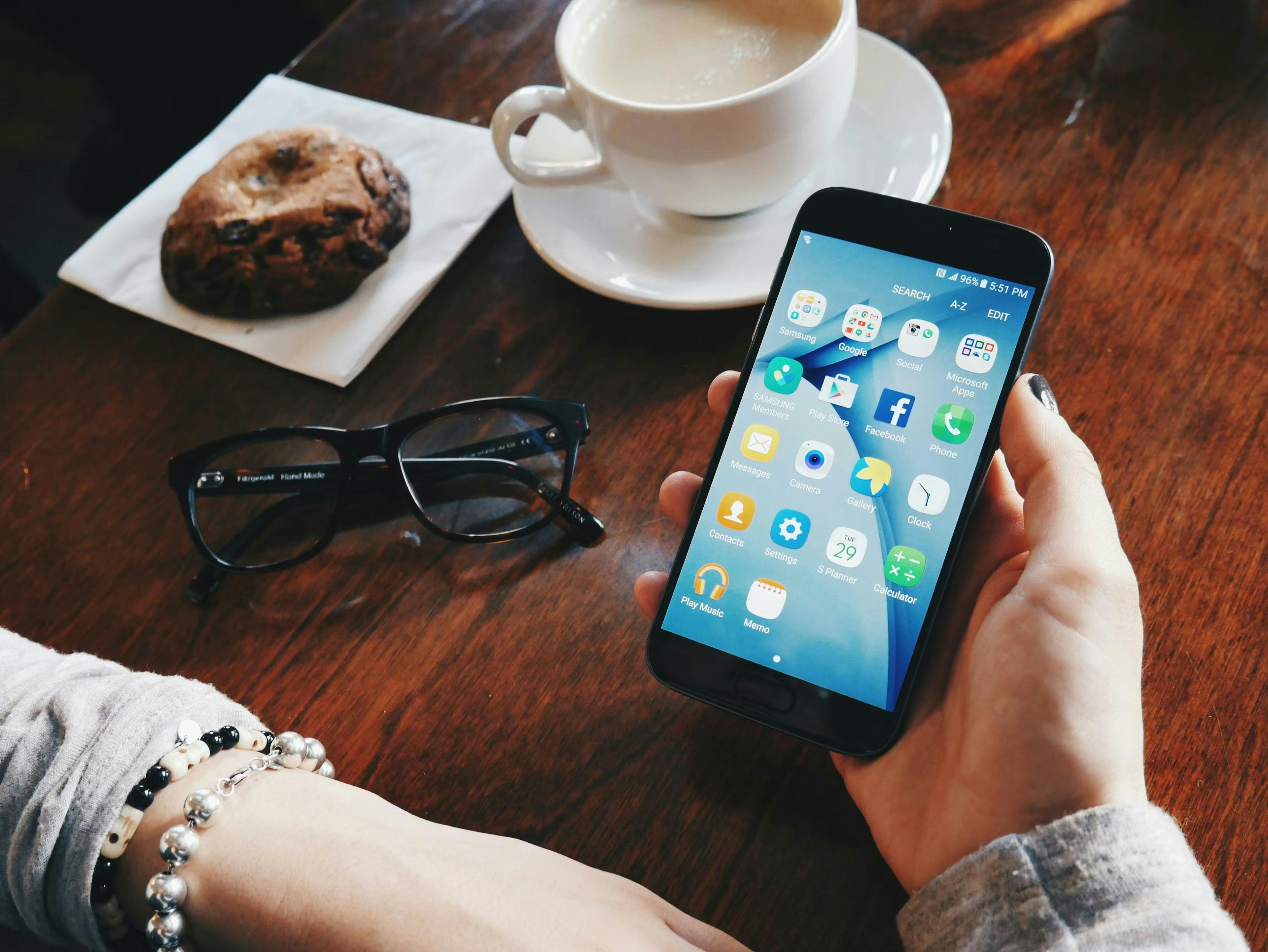A person holding a smartphone at a cafe table next to a coffee and cookie, demonstrating the need for a mobile responsive website and website speed optimization for users on the go.