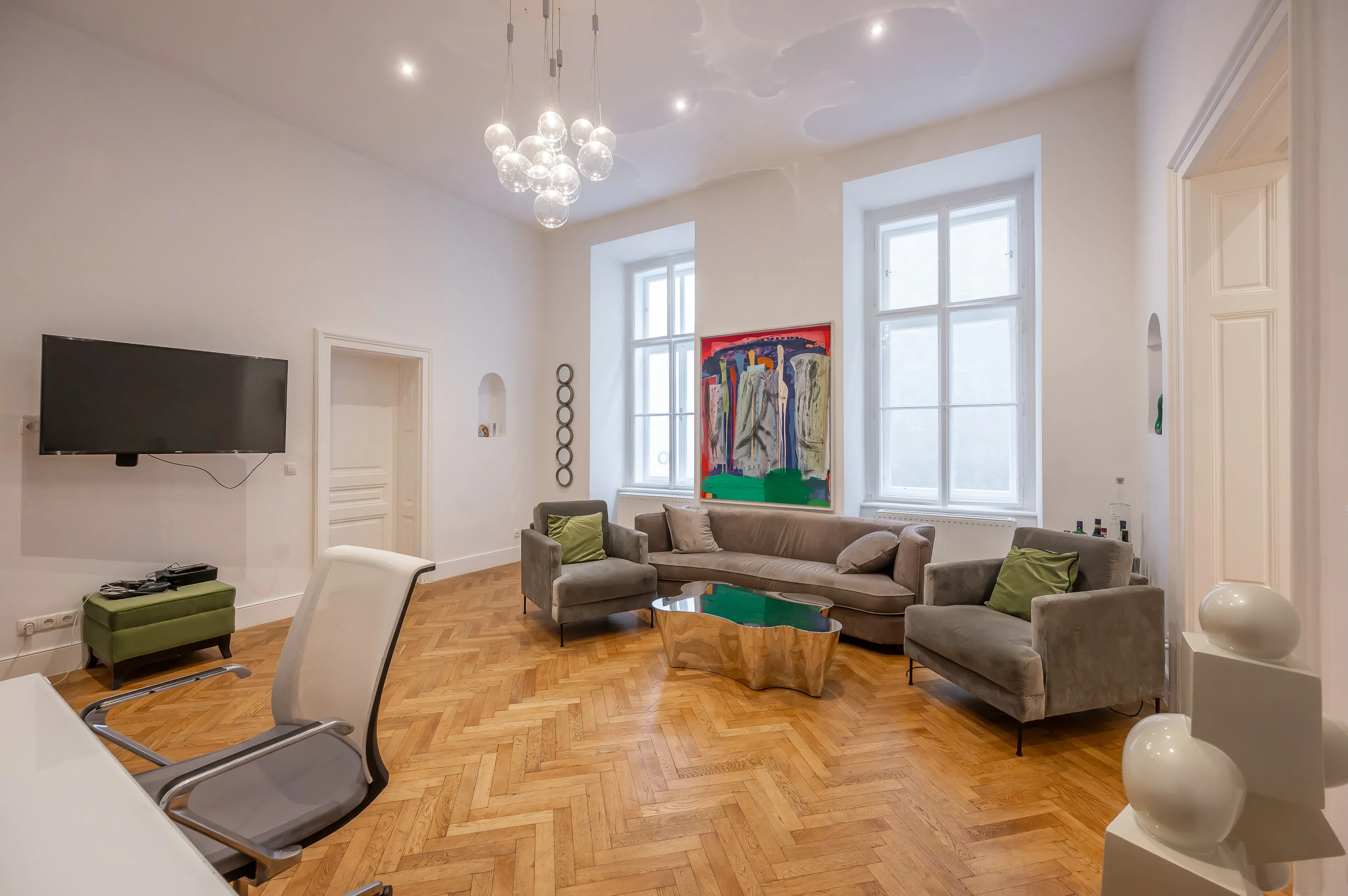 Eingerichtetes Wohnzimmer. Heller Fischgrätparkett, Sofa mit Couchtisch, Fernseher und buntes Bild an der Wand.