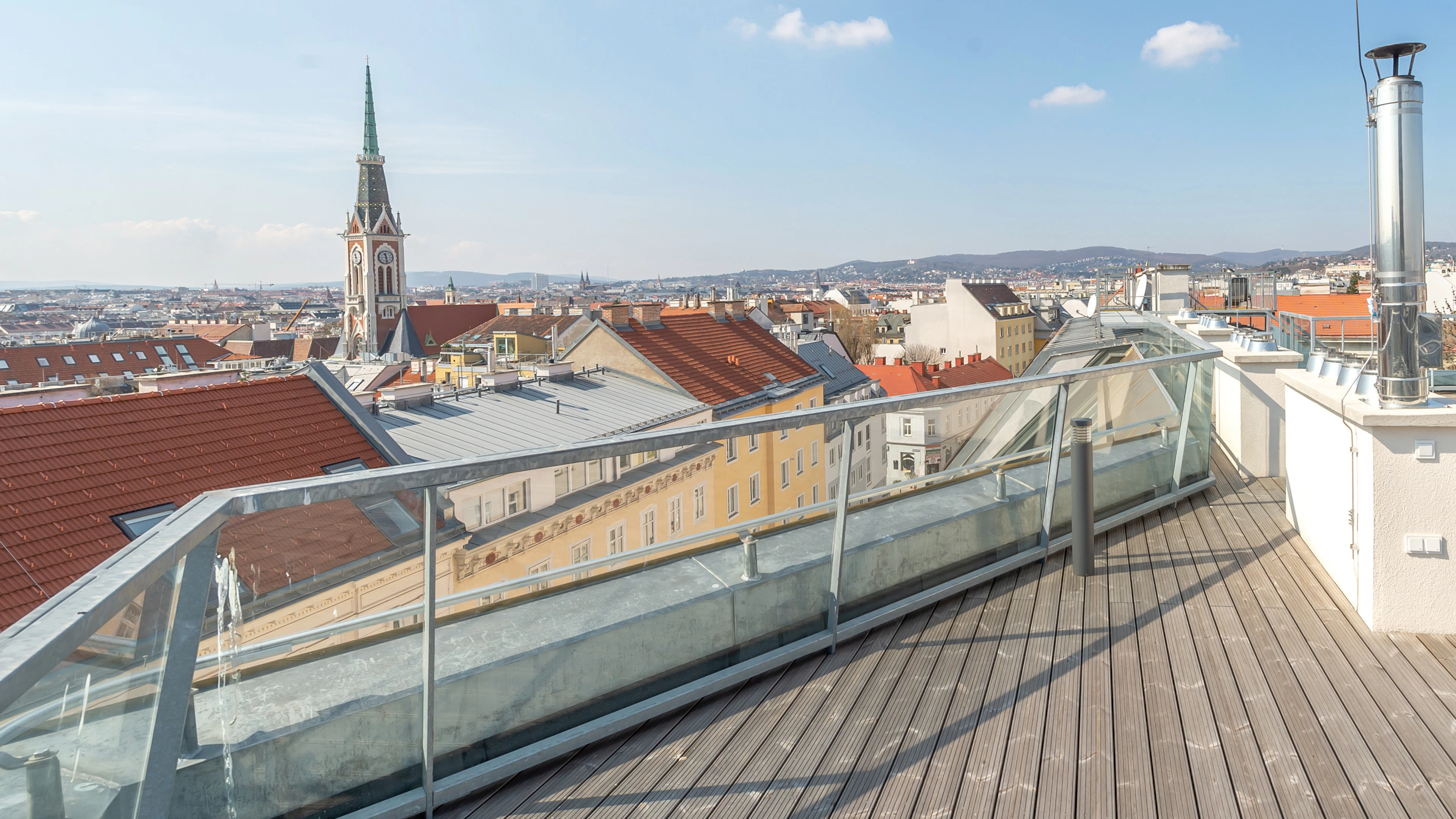 Große Dachterrasse mit Blick über Wien, eine Kirche ist im Hintergrund zu sehen.
