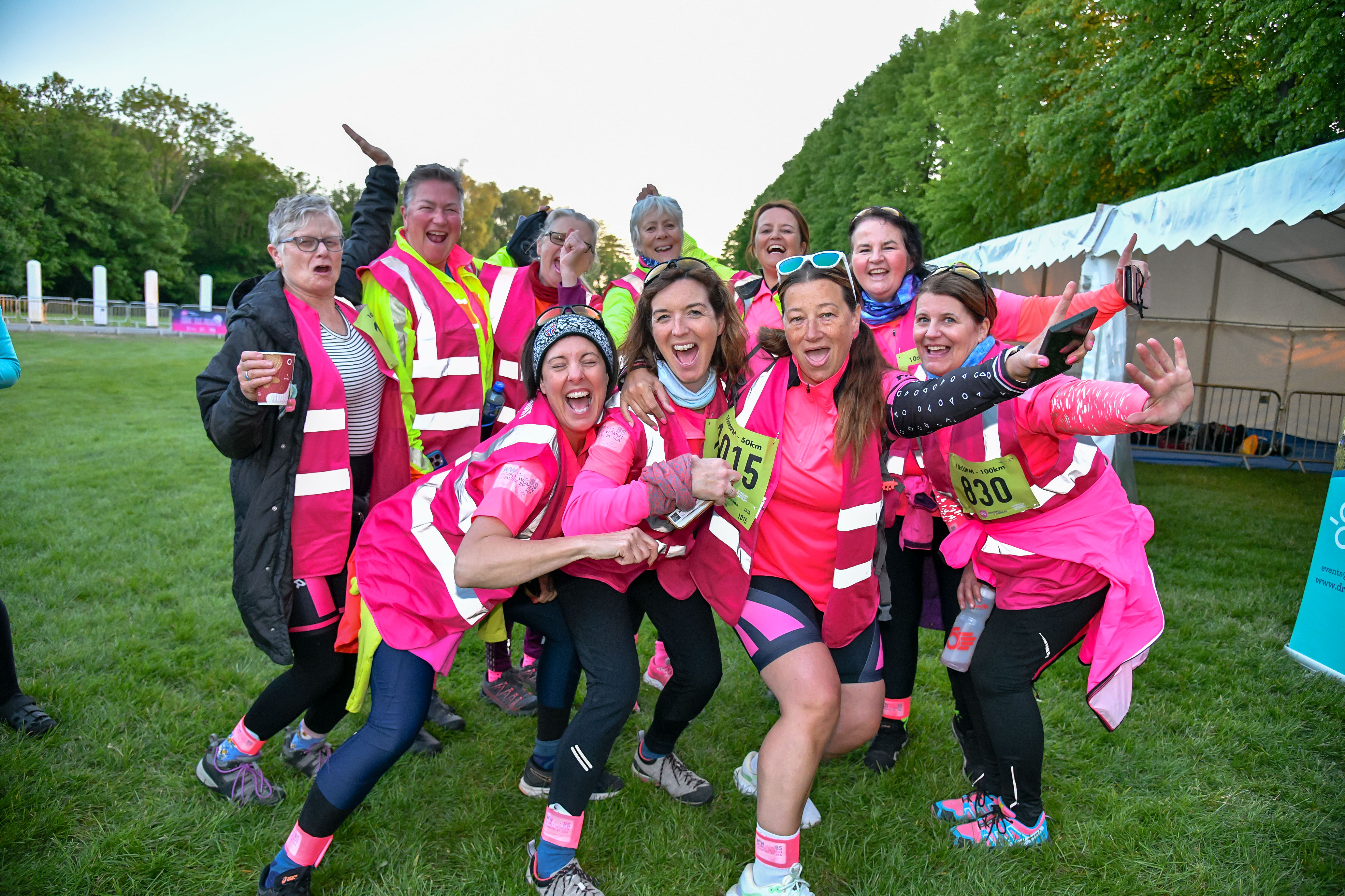 Group of six individuals dressed in high-visibility and neon-themed attire, posing together at an outdoor nighttime event. Their coordinated outfits include reflective vests, glowing footwear, and colourful accessories.