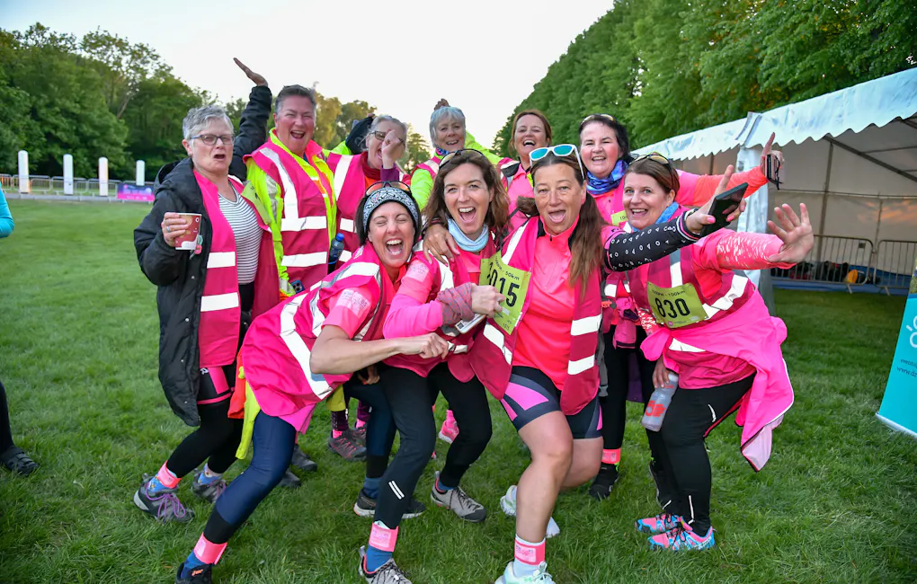 Group of six individuals dressed in high-visibility and neon-themed attire, posing together at an outdoor nighttime event. Their coordinated outfits include reflective vests, glowing footwear, and colourful accessories.