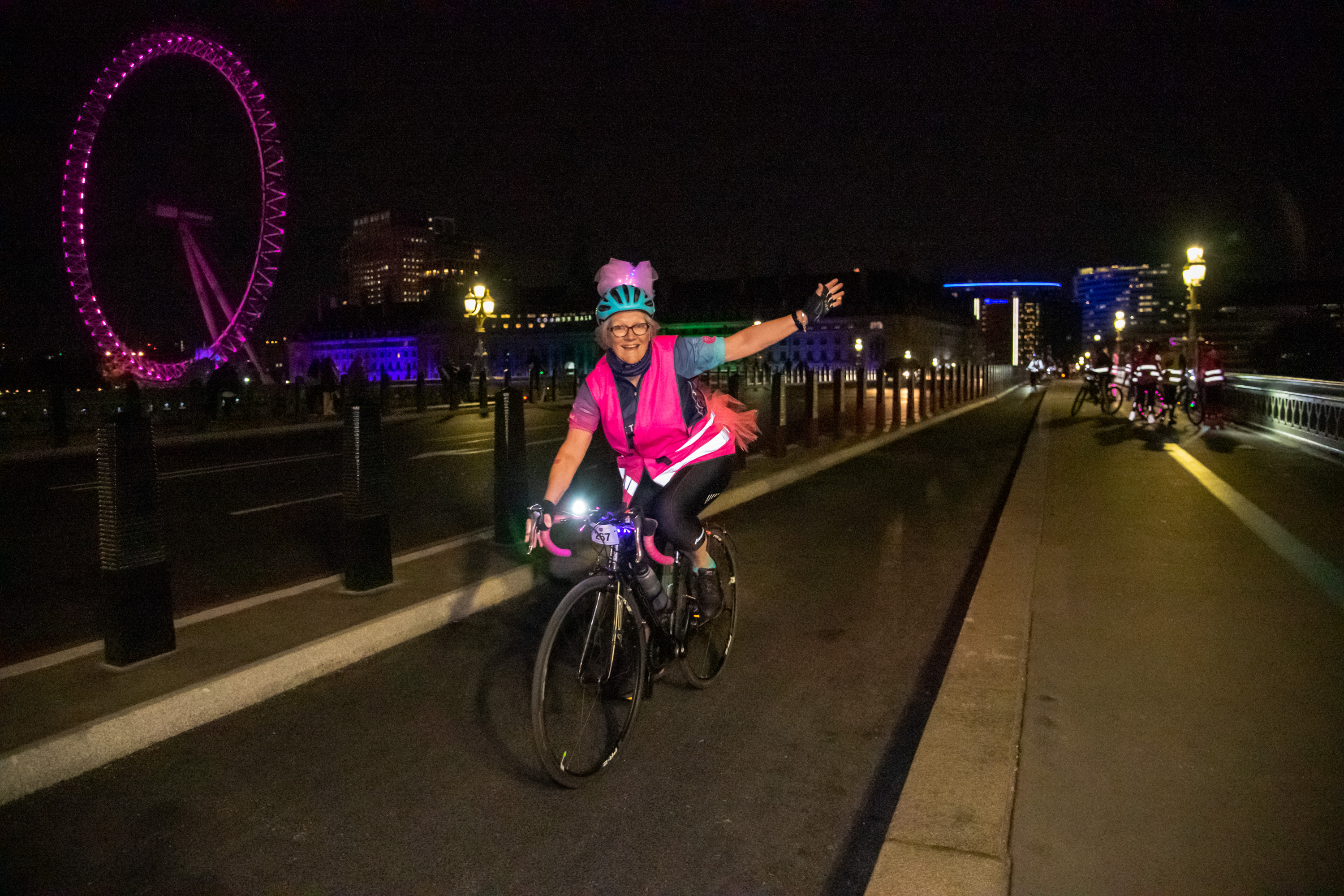 Smiling Ride the Night participant wearing glowing neon pink accessories on a bike.