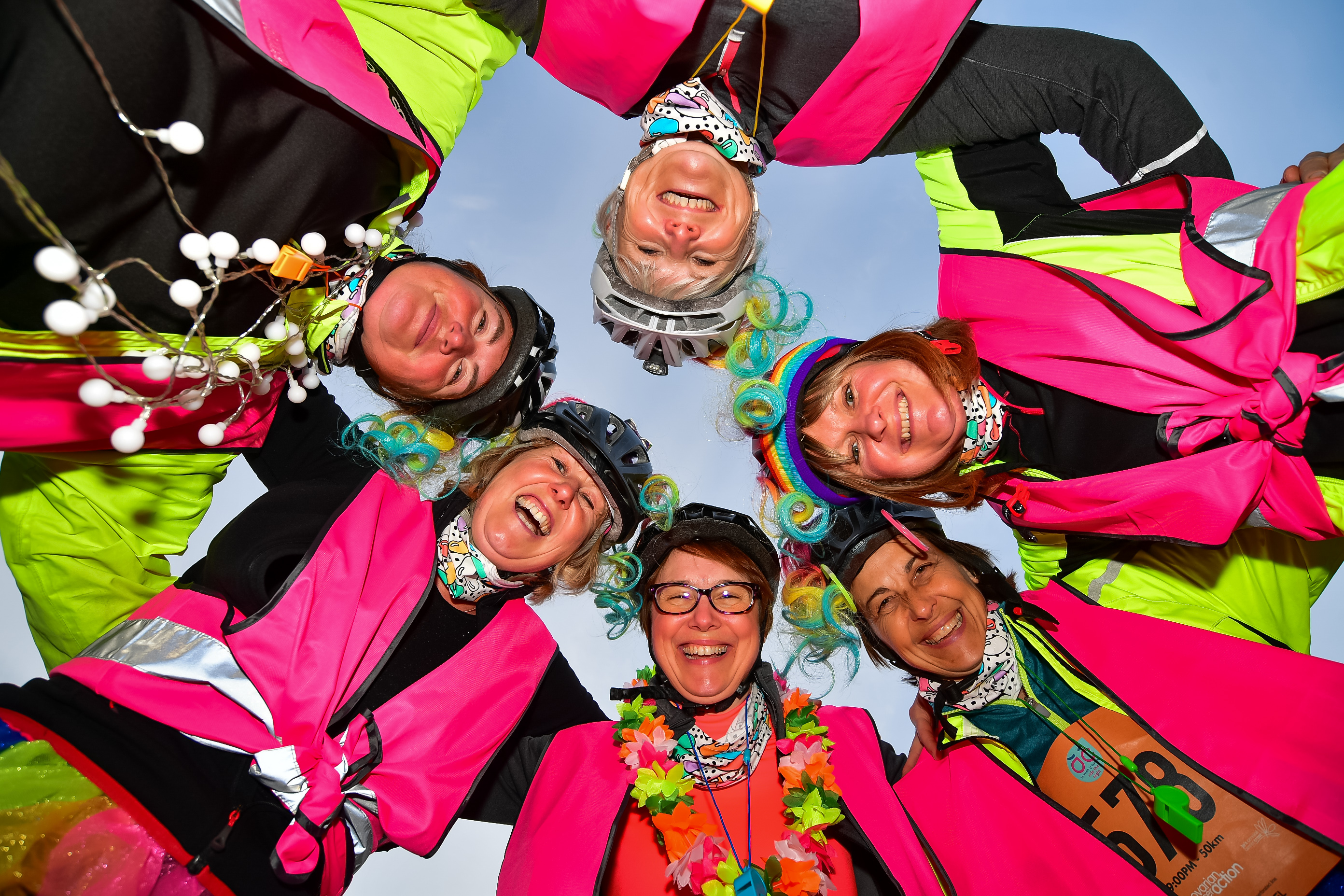 Group of Ride the Night participants in pink hi-vis jackets smiling down at the camera in a circle.