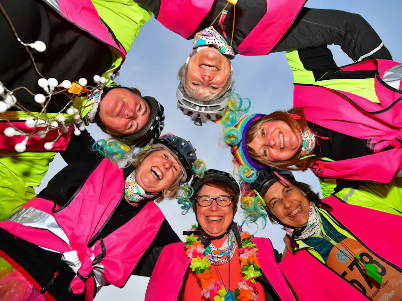 Group of Ride the Night participants in pink hi-vis jackets smiling down at the camera in a circle.