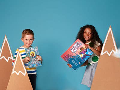 two children holding books behind carboard mountains