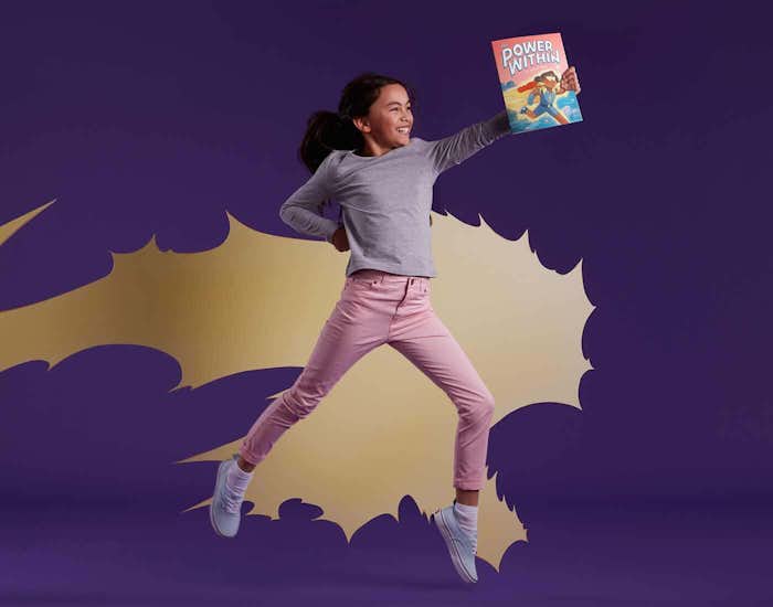 Child holding The Power Within book leaping through the air as an empowered super hero