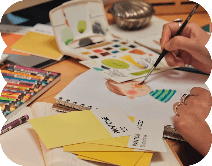 Artist painting with watercolors, surrounded by supplies.
