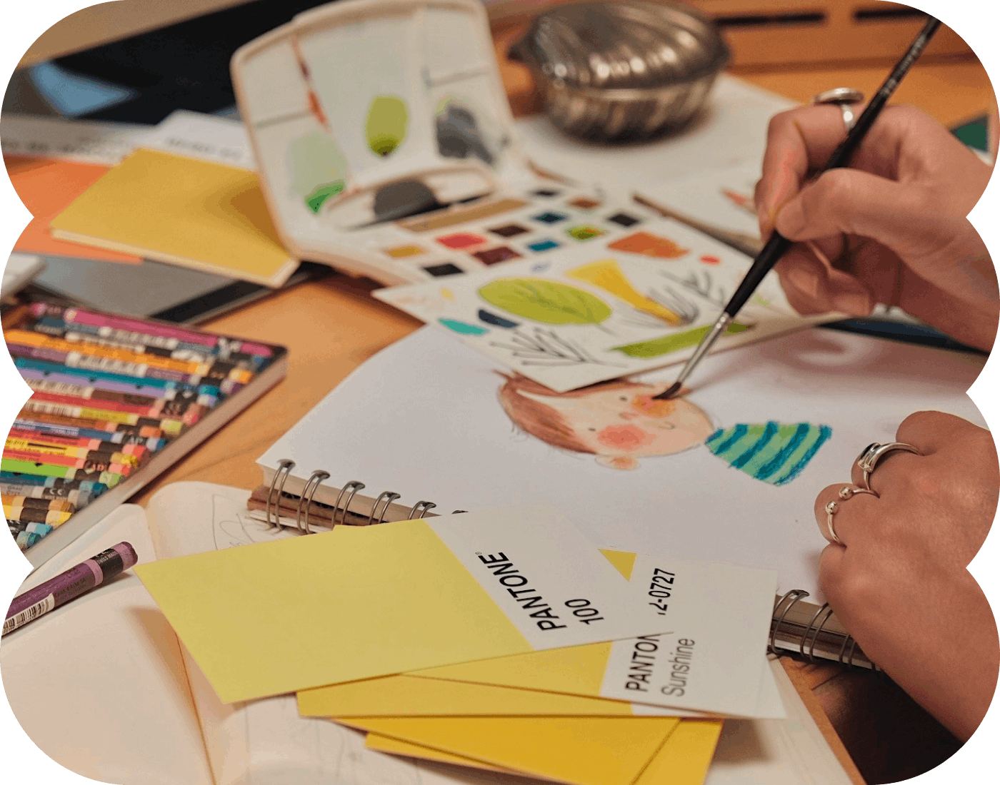The artist hands painting an avatar surrounded by pencils and paint