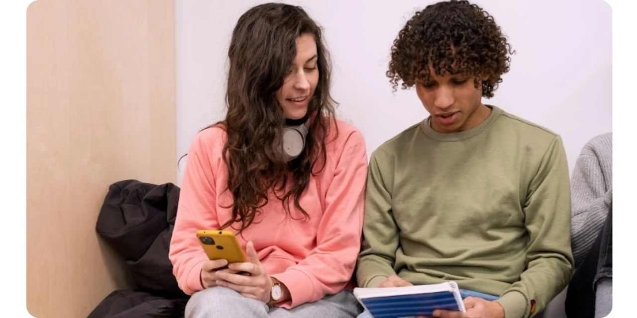 Deux étudiants révisent et discutent en utilisant leur téléphone et leurs notes.