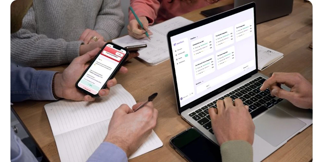 People taking notes at a table while checking training progress on a laptop showing the Wooflash dashboard and a phone displaying a Wooflash flashcard.