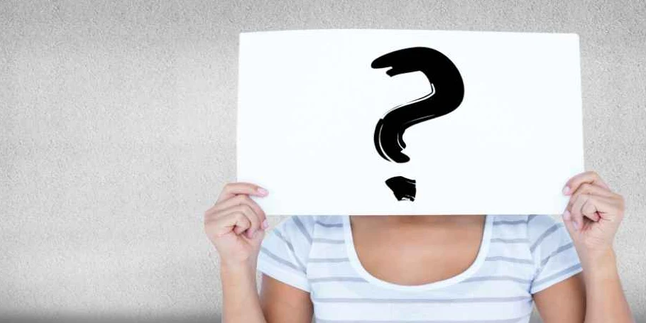 A person hides their face behind a white sign with a black question mark drawn on it