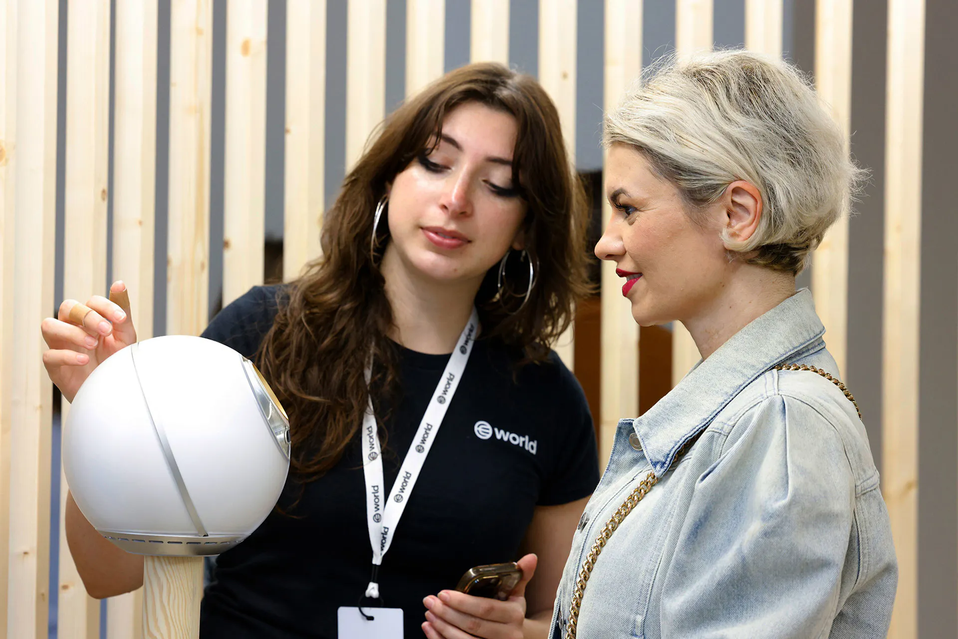 A woman explains how to use the Orb for World ID verification to another woman, who is attentively listening.