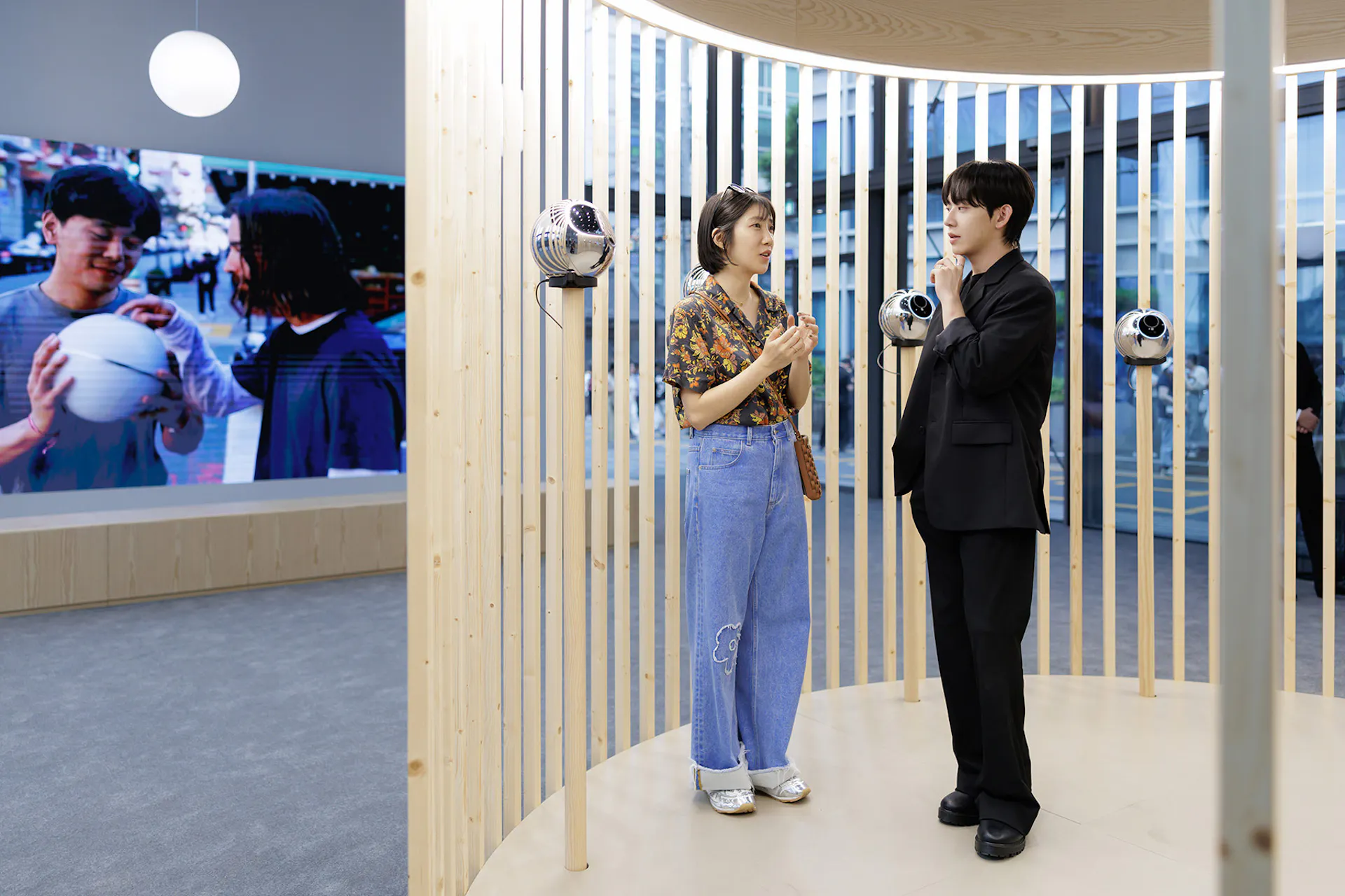 Two individuals engaging in conversation near biometric verification Orbs, with a digital screen displaying a community scene in the background.