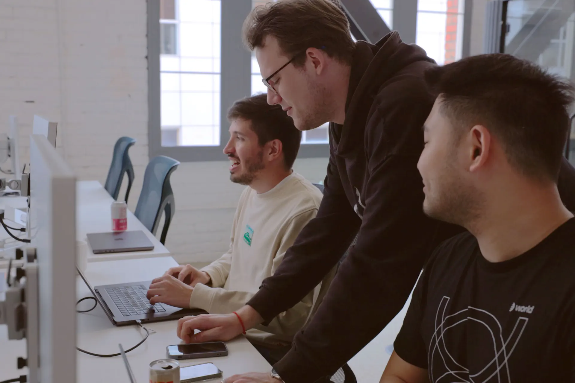 Three developers collaborating at desks, working on laptops in a bright workspace, celebrating the success of Mini Apps in the World ecosystem.