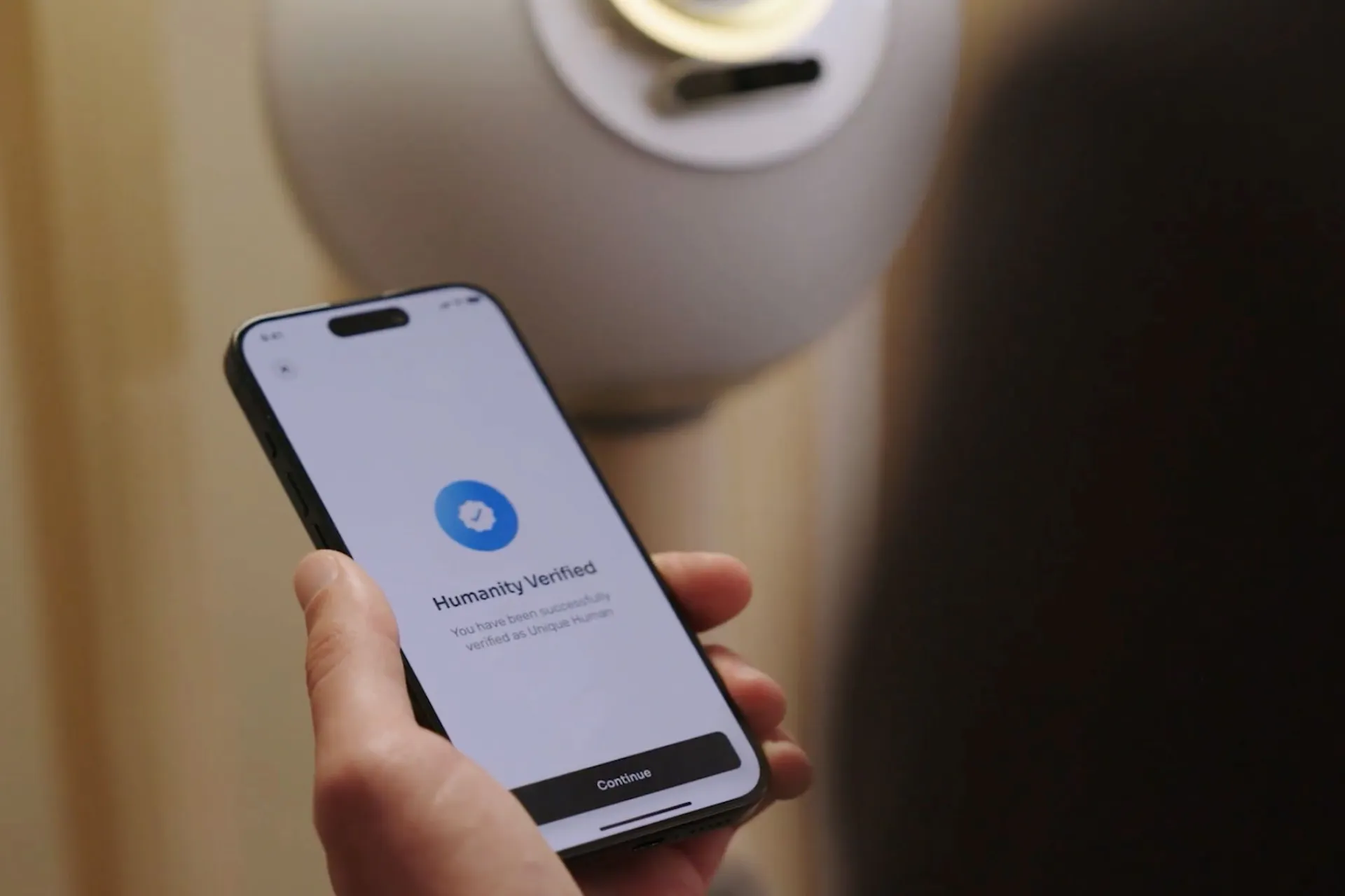 A person holding a smartphone displaying a 'Humanity Verified' message, with an Orb in the background.