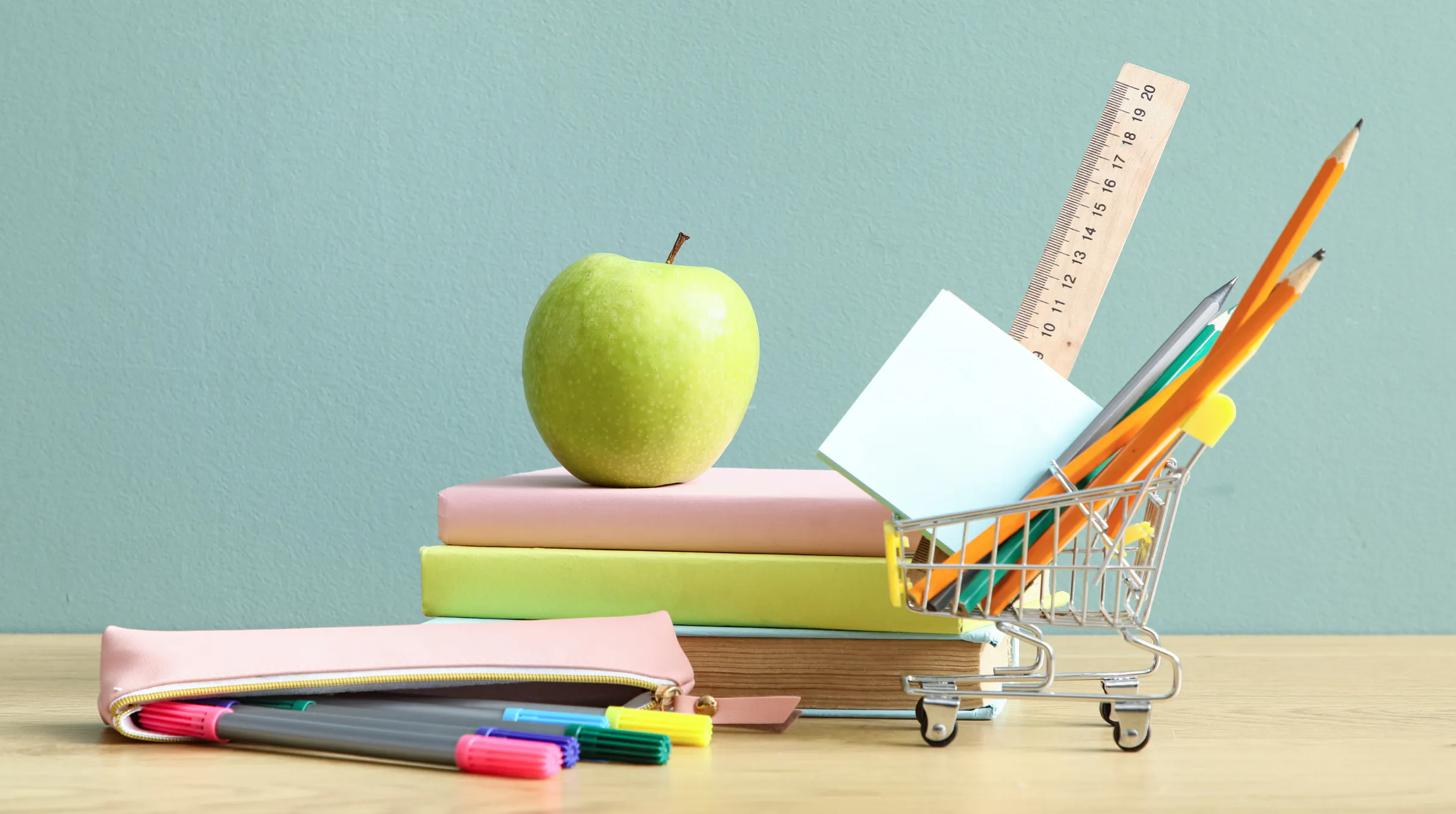 Back to school supplies including pens, books, sticky note, ruler, and an apple