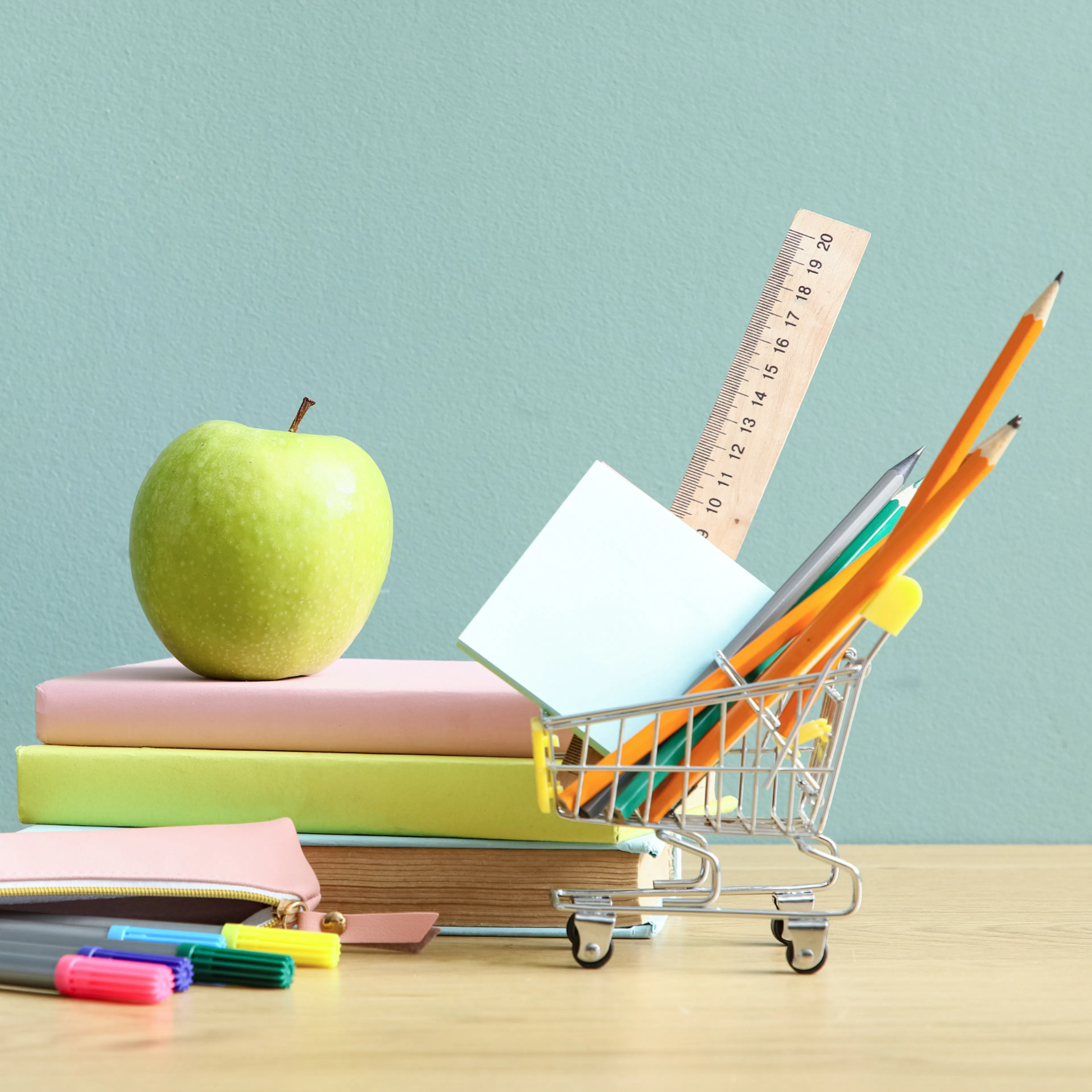 Back to school supplies including pens, books, sticky note, ruler, and an apple