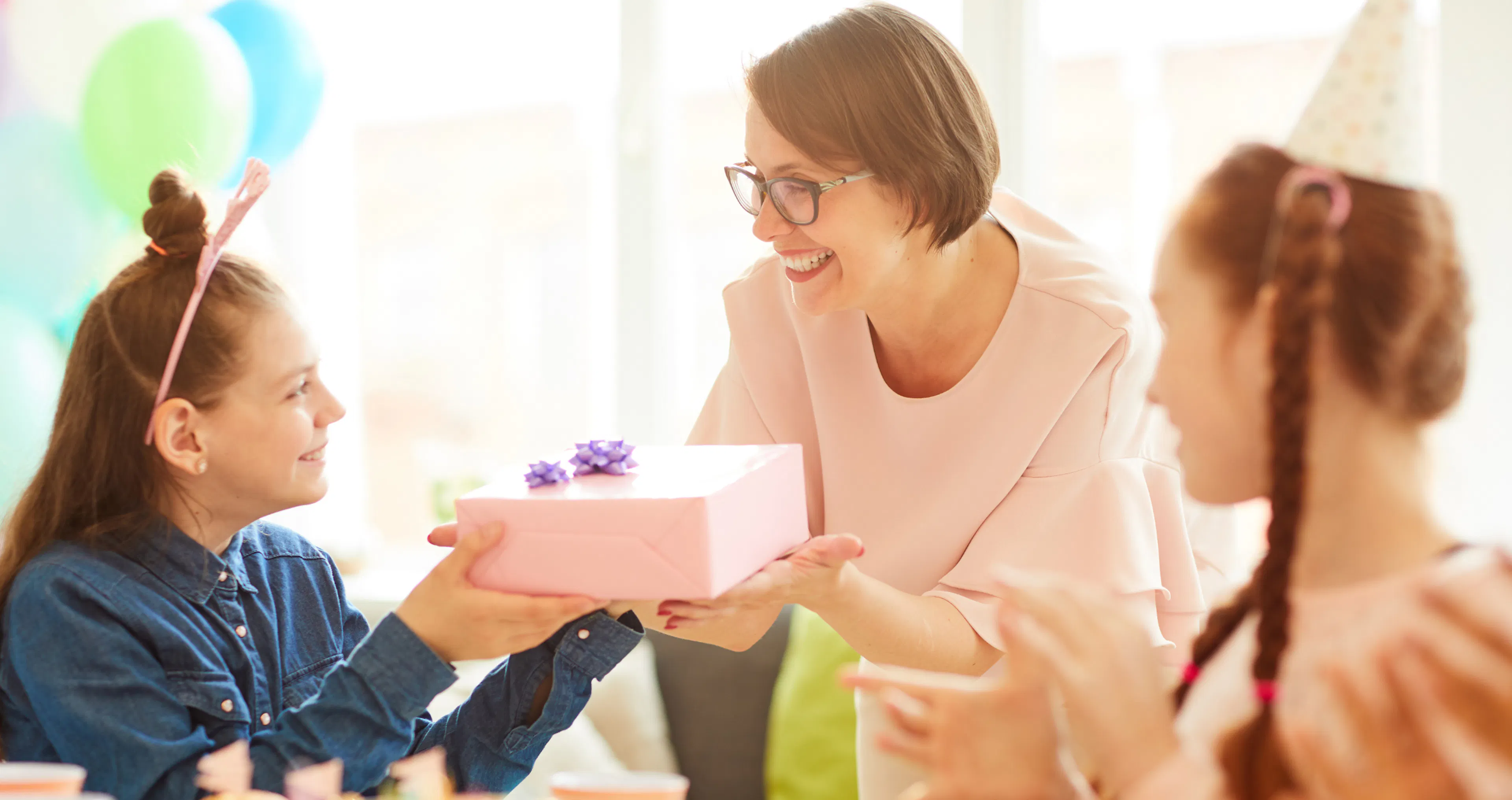Mother receiving a birthday gift from her daughters at a party with balloons and party hats