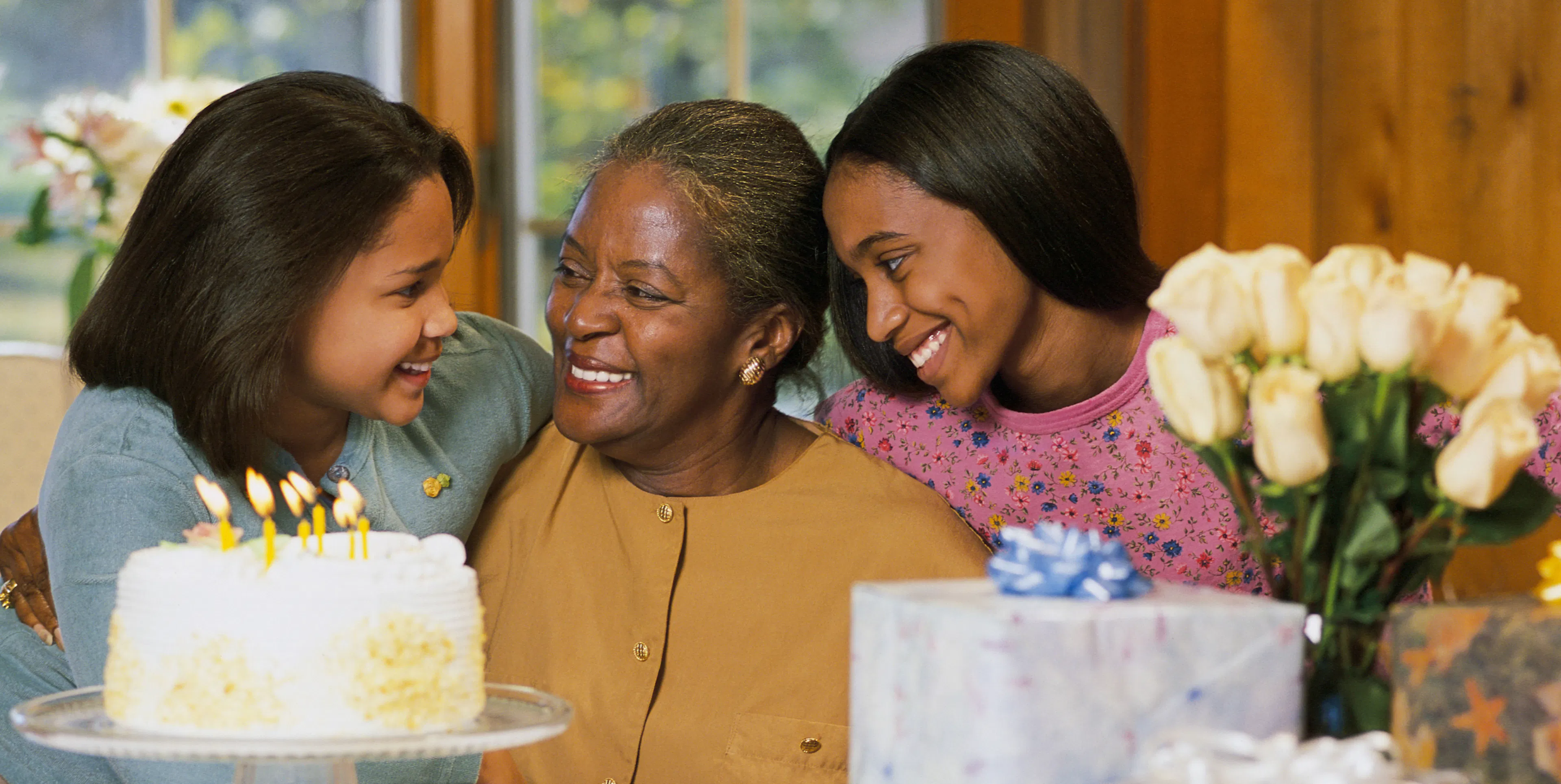 Three generations of women smiling together around a birthday cake with lit candles