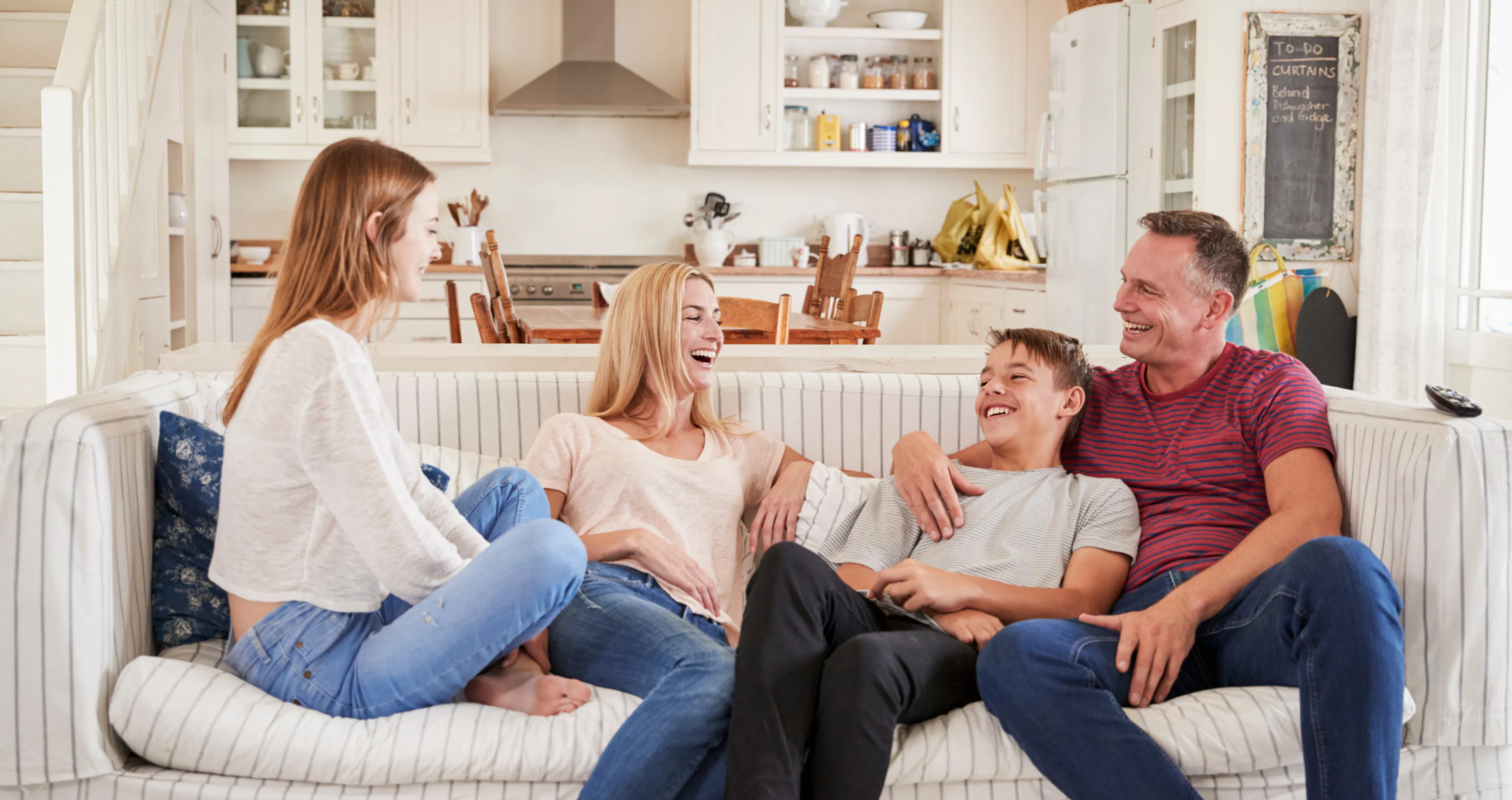 Family of four laughing together on a couch in their kitchen, enjoying screen-free time and reconnecting in real life