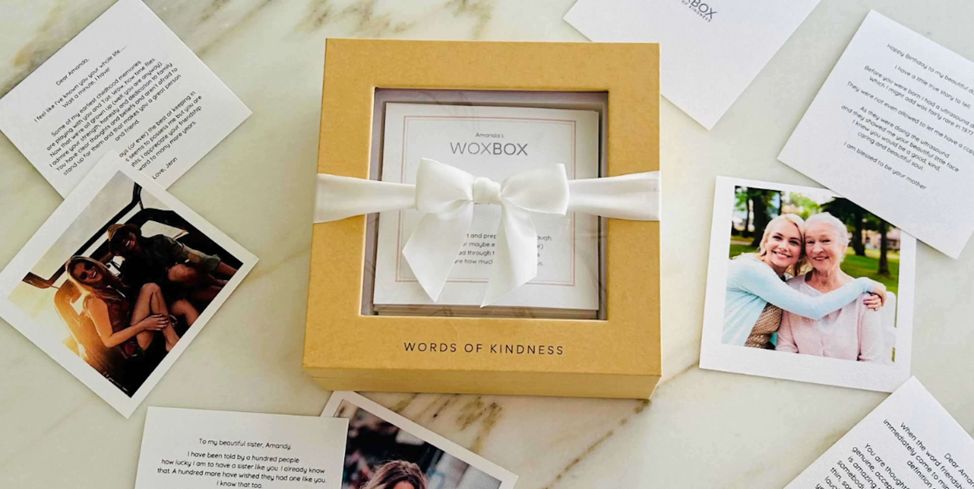 Printed notes and photos on a counter with a Woxbox wrapped in a white ribbon, as part of a group gift