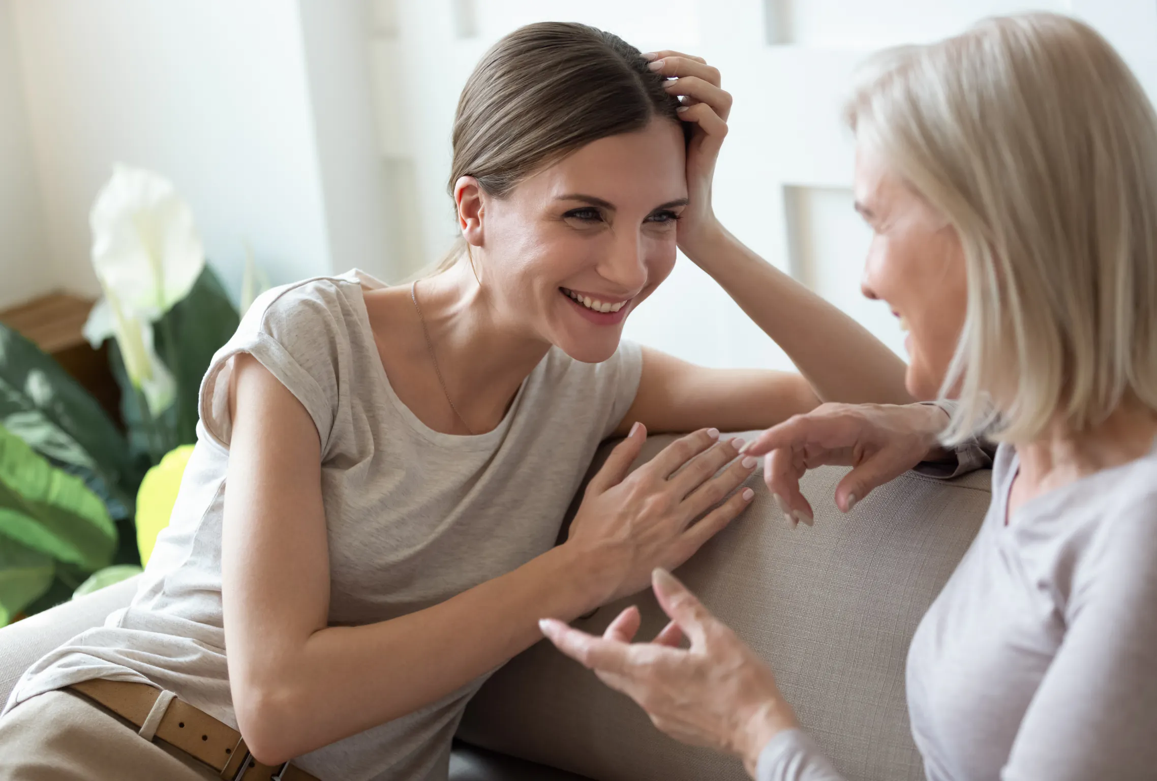 Younger woman laughing on a couch while talking with an older woman, showing the joy of friends of different ages