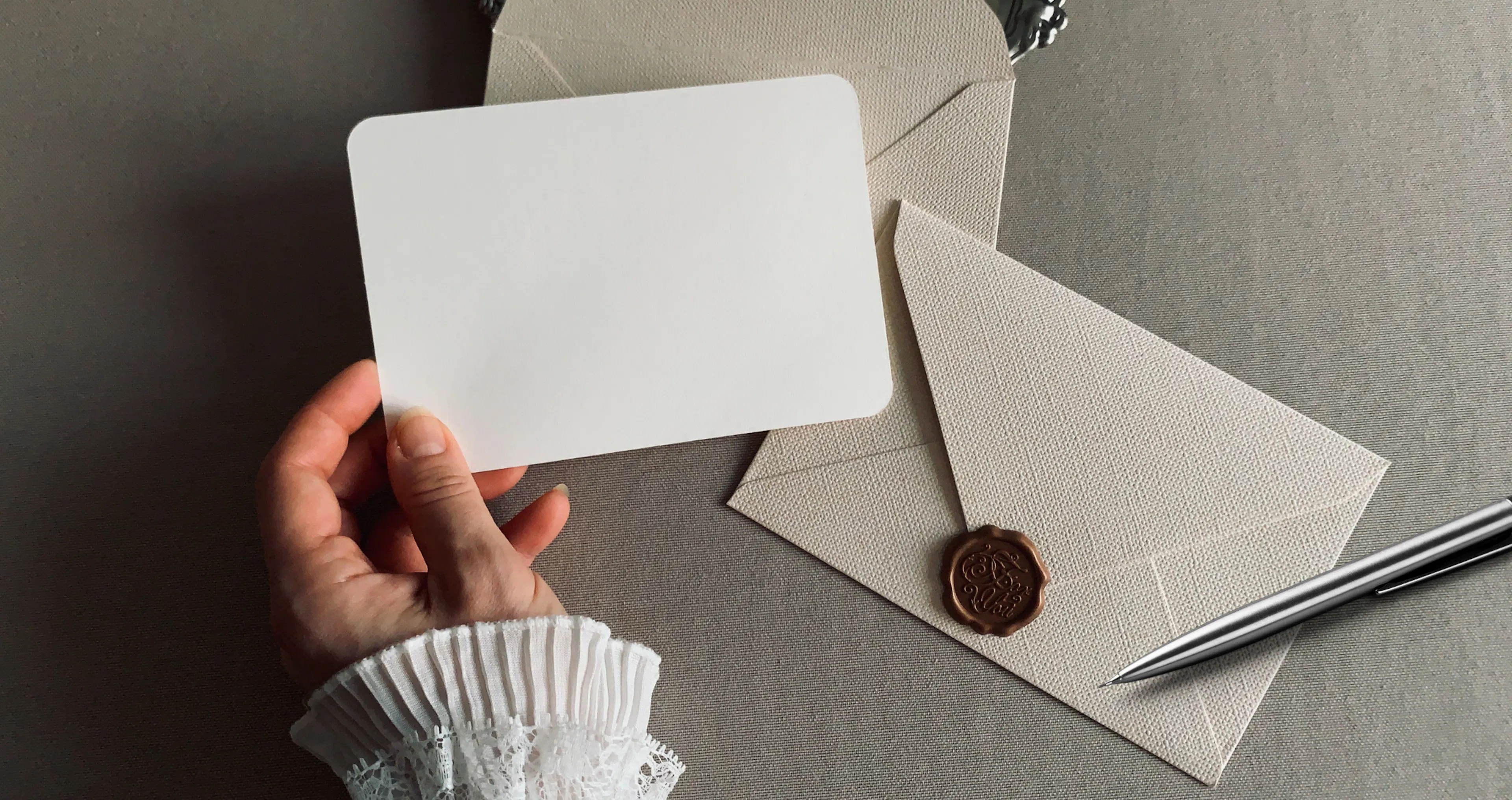 Hand holding a blank card beside a wax-sealed envelope and pen, ready for a heartfelt new beginning message
