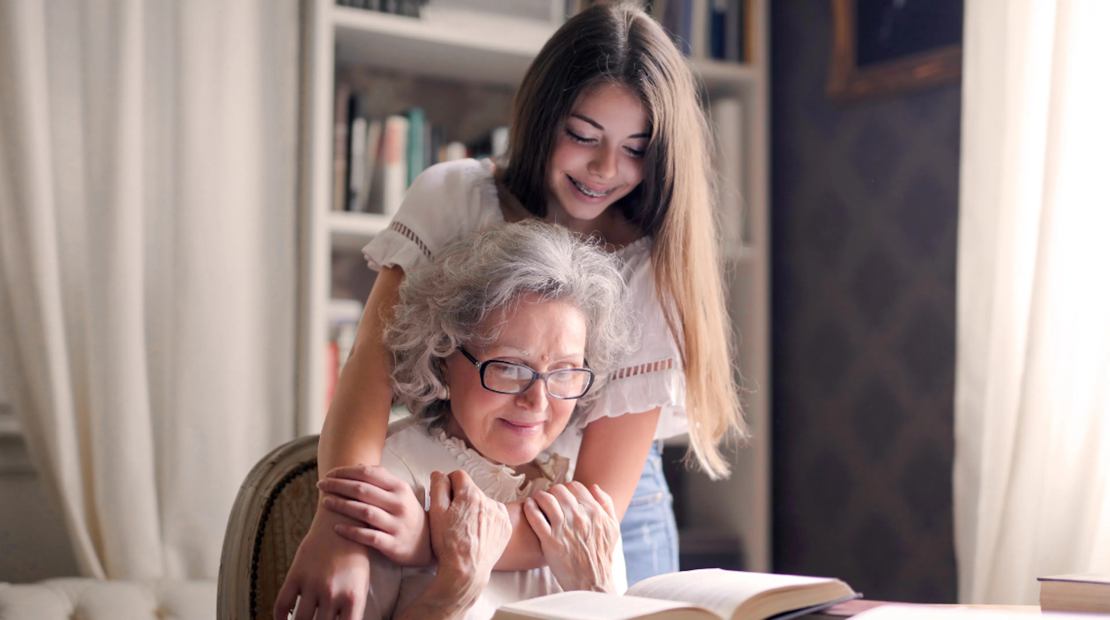Young woman hugging her grandmother while reading a book together