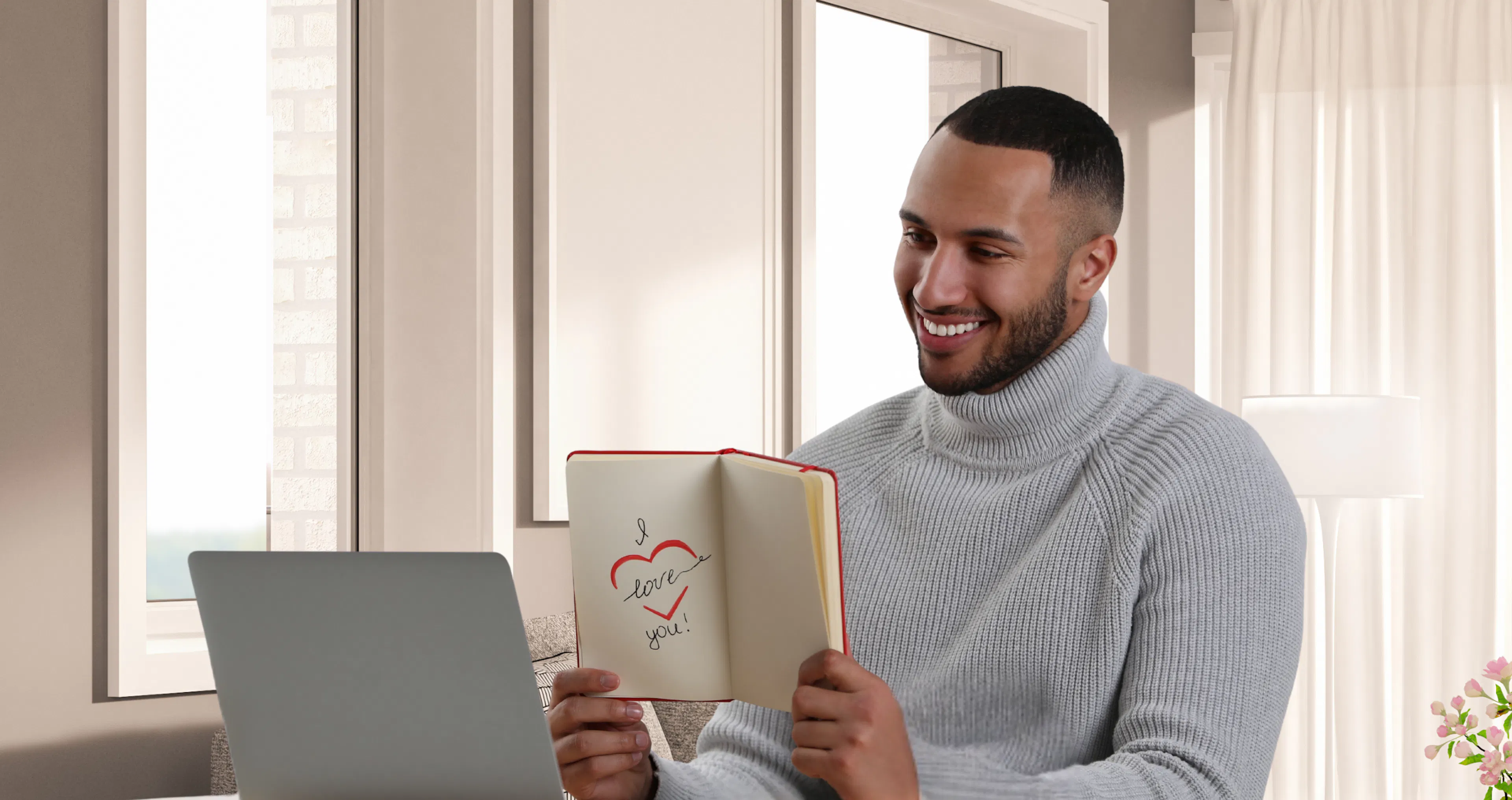 Man at his desk holding up a book that says “I love you” while smiling at a video call with his long-distance partner