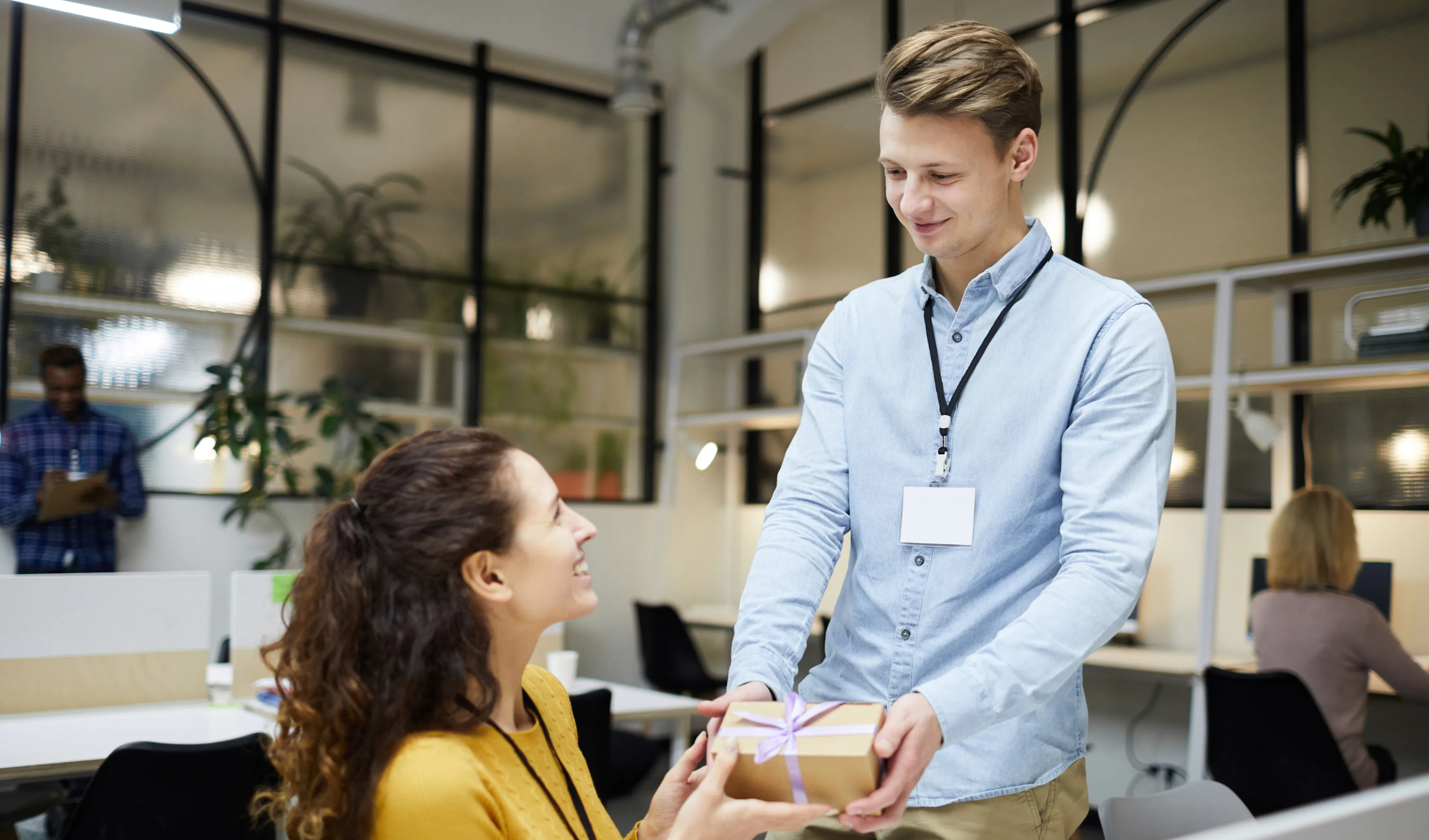 Employee presenting a ribboned group gift to a smiling colleague at her desk in the office
