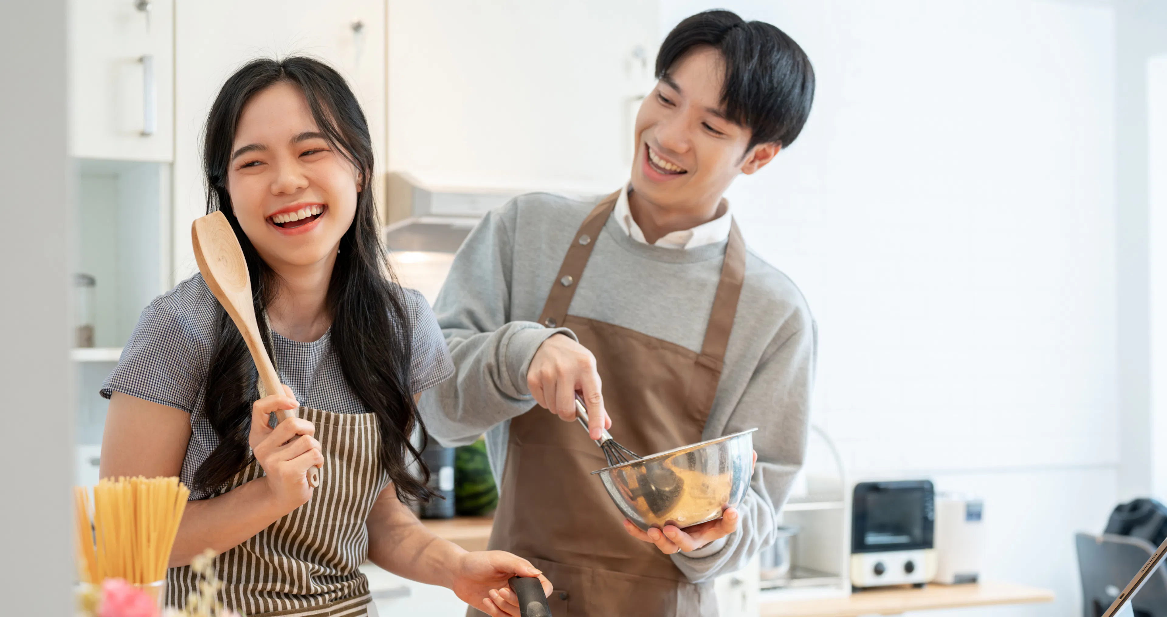 Laughing couple cooking together in a bright kitchen, enjoying quality time as a meaningful way to show appreciation