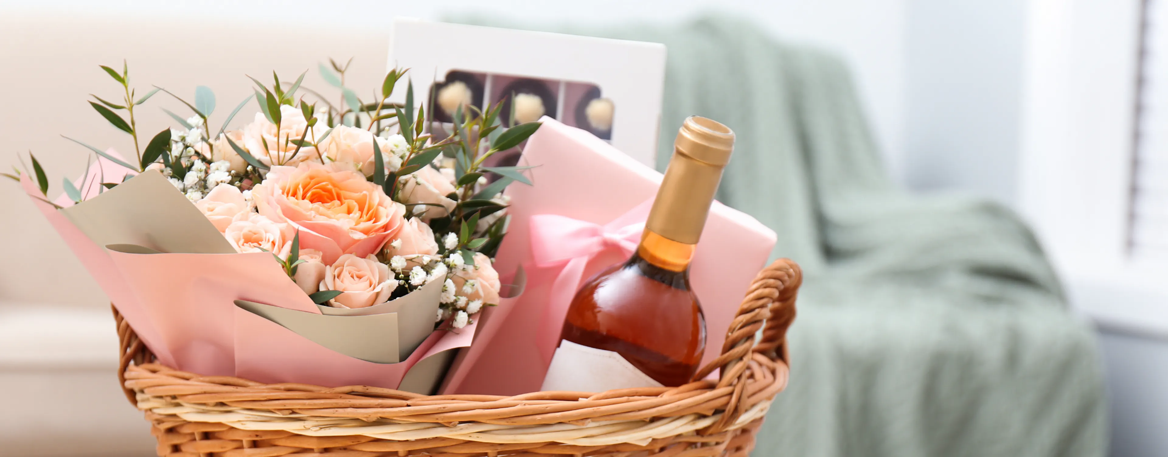 Assorted summer hostess gifts including wine, candles, and fresh flowers in a woven basket