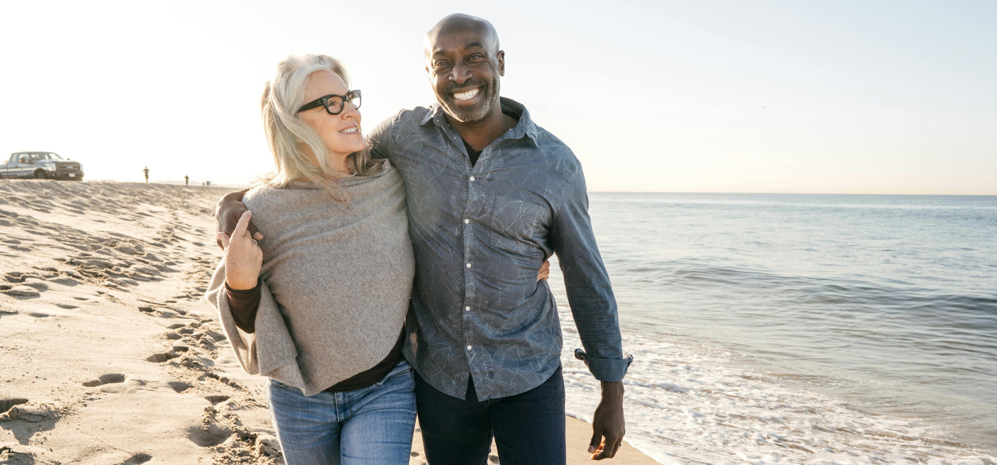 Newly retired couple walking on the beach at sunset, by Woxbox Gift