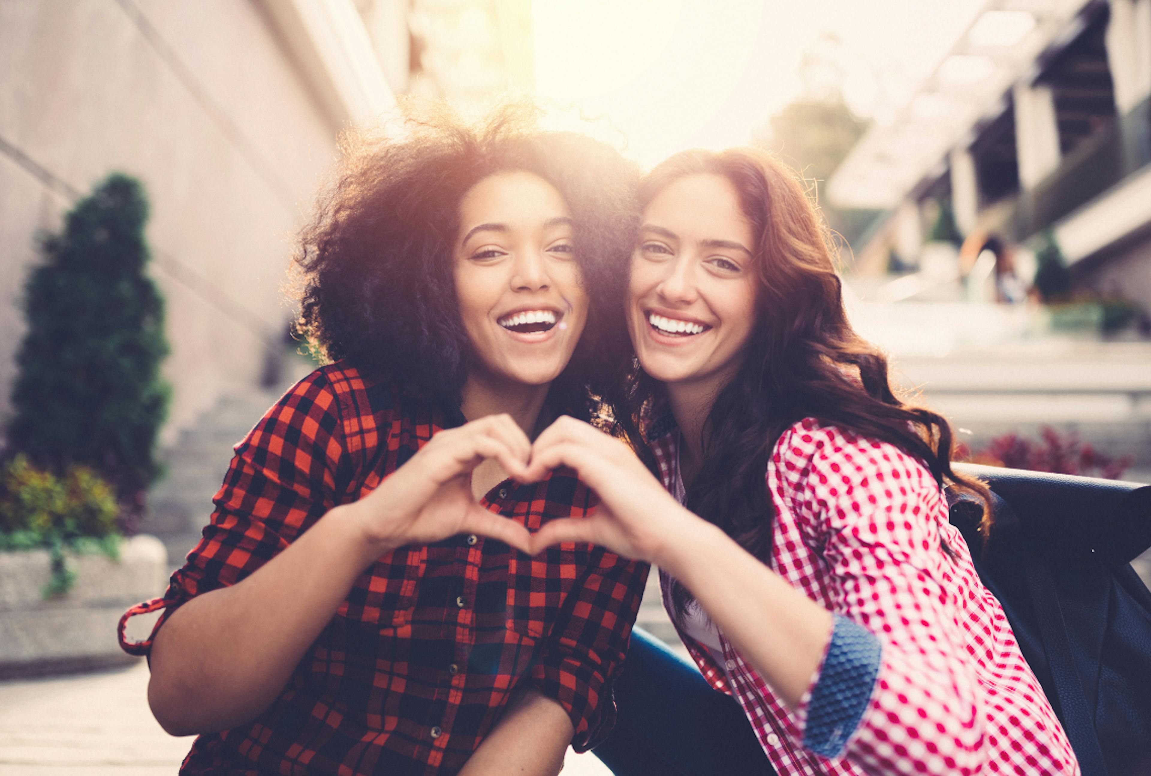 image of two friends smiling and holding their hands together to form a heart symbolizing friendship